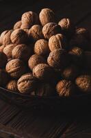 Heap of whole walnuts in shell in a bowl on brown wooden table. Vertical photo