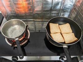 A pot of boiling water and bread toast on a Teflon pan. photo