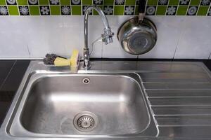 The clean metal sink with the chrome tap after washing on the modern counter. photo