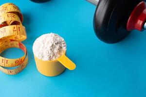 A scoop of creatine next to a dumbbell and a tape measure on a blue background. photo