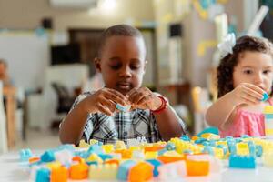 africano pequeño chico preescolar jugando con de colores bloques en un jardín de infancia foto