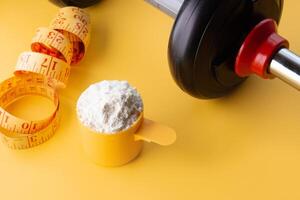 A scoop of creatine next to a dumbbell and a tape measure on a yellow background. photo