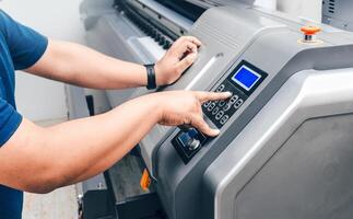 unrecognizable man manipulating or controllingbuttons from a large format printing press. photo