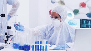 Chemist in a modern science laboratory using blue liquid for test. Chemical reaction. Scientist in coverall protection equipment. video