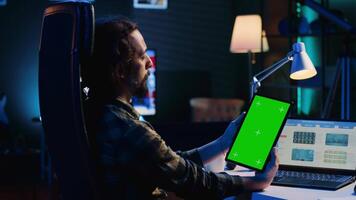 remotamente trabajando hombre en hogar oficina cheques estadístico financiero gráficos en computadora portátil, comprobación cruzada con datos en croma llave tableta. persona de libre dedicación participación aislado pantalla dispositivo, analizando negocio gráficos video