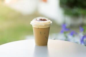 Cappuccino with ice in a clear plastic glass on a white table with a natural atmosphere. photo