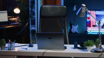 Panning shot of personal office desk in front of smart TV displaying news program broadcasting. Laptop and business documents on table and television screen in empty room showing VOD channel video