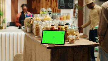 Greenscreen display shown on tablet at neighborhood grocery store, support low carbon footprint and eco friendly farming. Gadget with blank copyspace layout next to bulk items in jars. Camera A. video