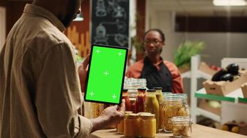 African american client holding tablet with greenscreen layout in local organic shop, looking at chromakey next to additives free goods. Regular customer uses device with isolated copyspace. Camera A. video