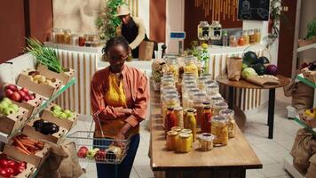 africain américain acheteur en mettant Pâtes et biologique sauce dans une panier, choisir végétalien éthiquement source nourriture alternatives. femme achat éco amical Naturel des produits de local épicerie magasin. caméra b. video