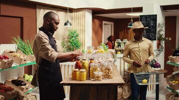 African american farmer opening local zero waste store with natural additives free bulk products and homegrown produce. Merchant preparing goods in reusable jars at eco supermarket. Camera B. video