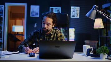 controlo remoto empregado trabalhando às casa escritório mesa, lendo em formação em computador portátil e escrevendo dentro caderno. trabalhador autonomo anotando baixa Ideias em papel usando caneta enquanto teletrabalho, Câmera b video