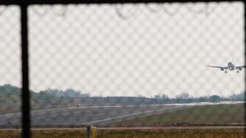 Footage of an airplane with an unrecognizable livery, landing, touching and braking. View of the runway through the airport fence. Airstrip video