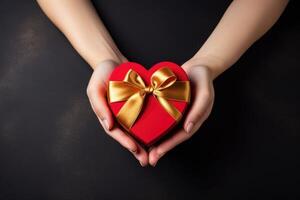 ai generado mujer manos tiernamente sostener un rojo en forma de corazon regalo caja con un oro cinta, ai generado. foto