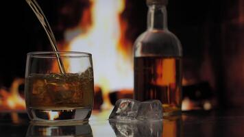 Pouring whiskey or scotch from a Bottle to a Glass over Fireplace background. Warmth and home comfort. 4K video