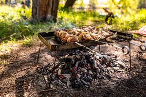 Barbecue at a picnic with grilled kebabs. Half-cooked pieces of pork meat on skewers on an old iron portable grill over coals photo