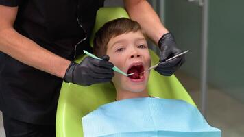 une mignonne garçon avec un ouvert bouche est à la recherche à le côté tandis que le médecin est traiter sa les dents video