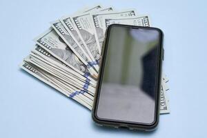 a smartphone and a stack of money on a blue background photo