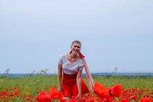 Blonde young woman in red skirt and white shirt, red earrings is in the middle of a poppy field. photo