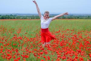 Blonde young woman in red skirt and white shirt, red earrings is in the middle of a poppy field. photo