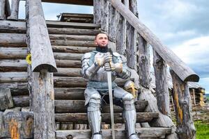 Knight in the armor on the wooden steps. Knightly armor and weapon photo