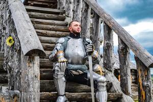 Knight in the armor on the wooden steps. Knightly armor and weapon photo