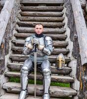 Knight in the armor on the wooden steps. Knightly armor and weapon photo