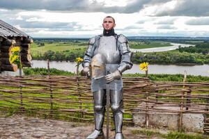 Knight in armor on the background of a wicker fence, a wooden house and the expanses of the motherland. photo