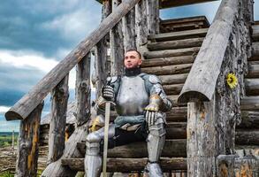 Knight in the armor on the wooden steps. Knightly armor and weapon photo