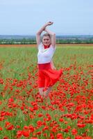 Blonde young woman in red skirt and white shirt, red earrings is in the middle of a poppy field. photo