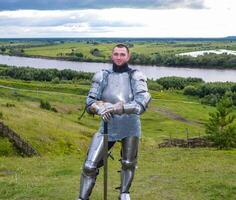 knight in armor stands against the background of native open spaces, forests and a river. Knightly armor and weapon photo