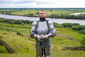 knight in armor stands against the background of native open spaces, forests and a river. Knightly armor and weapon photo