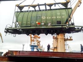 Russia, Novorossiysk 2021. Moving freight railway car in the port by a port crane. Cargo lifting operations. Industrial port photo