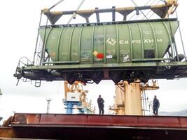 Russia, Novorossiysk 2021. Moving freight railway car in the port by a port crane. Cargo lifting operations. Industrial port photo