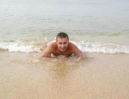 man on the shore lies. The sea wave covers the masculine. Beach photo