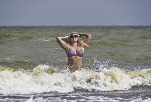 Beautiful blonde standing in sea water. Girl with sunglasses on photo
