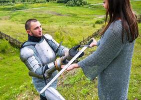 A lady in a chain mail hands a sword to her knight in armor. photo