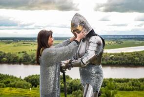 The lady puts on her knight a helmet. Knightly armor and weapon photo