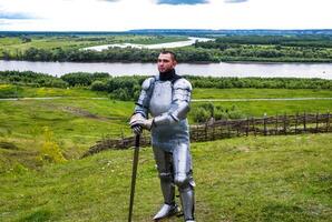 knight in armor stands against the background of native open spaces, forests and a river. Knightly armor and weapon photo