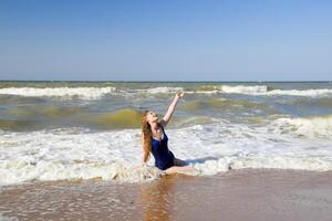 A blonde girl in a blue bathing suit on the beach. Beach holidays. photo