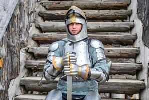 Knight in the armor on the wooden steps. Knightly armor and weapon photo