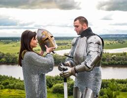 The lady puts on her knight a helmet. Knightly armor and weapon photo