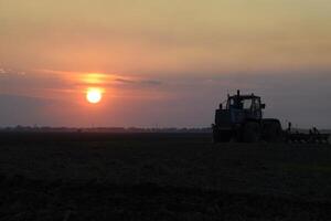 Tractor plowing plow the field on a background sunset. tractor silhouette on sunset background photo