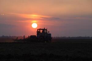 Tractor plowing plow the field on a background sunset. tractor silhouette on sunset background photo