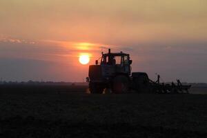 Tractor plowing plow the field on a background sunset. tractor silhouette on sunset background photo