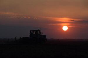 Tractor plowing plow the field on a background sunset. tractor silhouette on sunset background photo