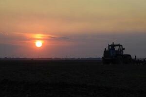 Tractor plowing plow the field on a background sunset. tractor silhouette on sunset background photo