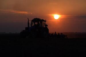 Tractor plowing plow the field on a background sunset. tractor silhouette on sunset background photo