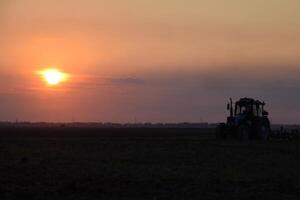 Tractor plowing plow the field on a background sunset. tractor silhouette on sunset background photo