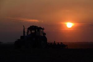 tractor arada arado el campo en un antecedentes puesta de sol. tractor silueta en puesta de sol antecedentes foto